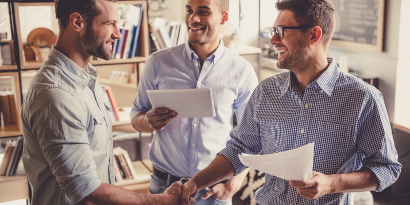 Three men holding paperwork, two of them shaking hands. 