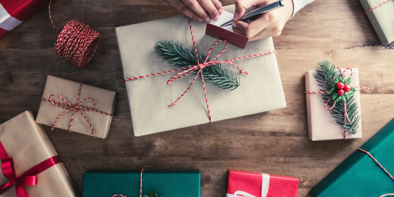 Person wrapping a gift and writing on a gift tag. 