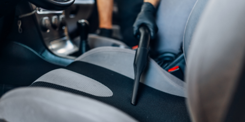 Person vacuuming a car seat.