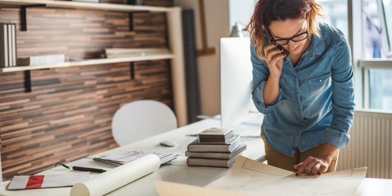 Interior designer on a call with a client standing near a desk.