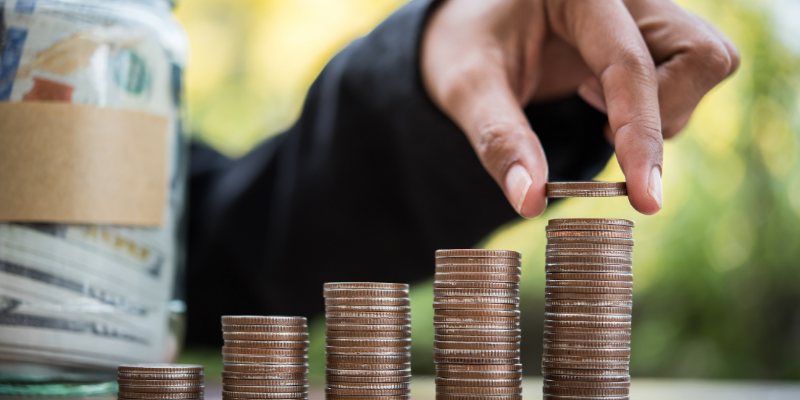 Man stacking coins next to a money jar.