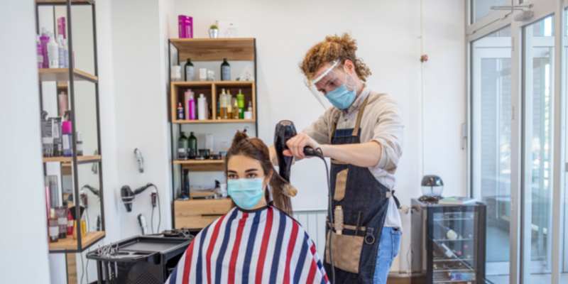 Hair stylist working on customer while they both wear masks.