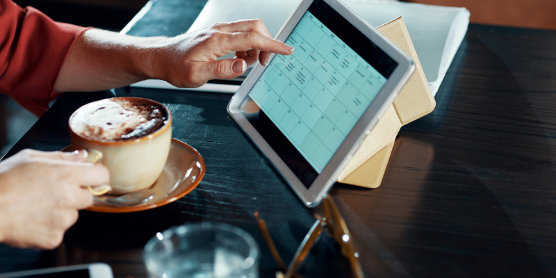 Business owner looking at her calendar on a computer pad while drinking coffee.