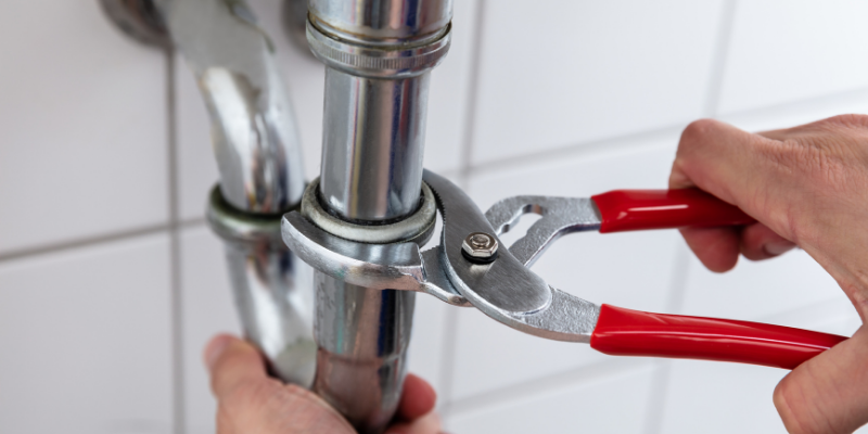 Person using pliers to remove a pipe fitting.