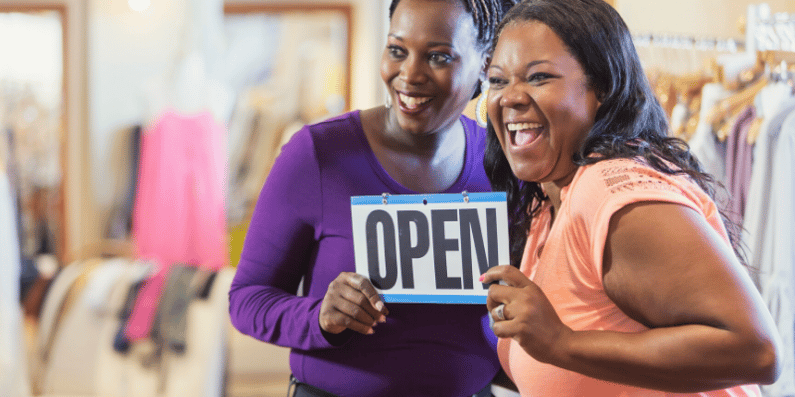 Two women holding an open for business sign.