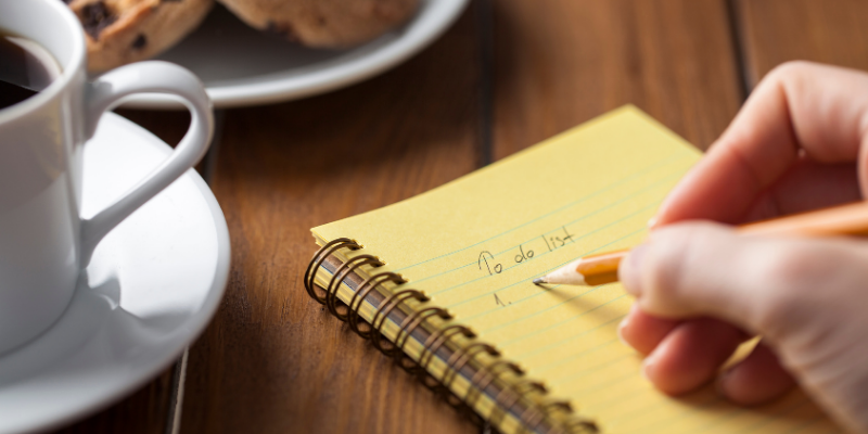 person writing a to-do list on a yellow notepad.