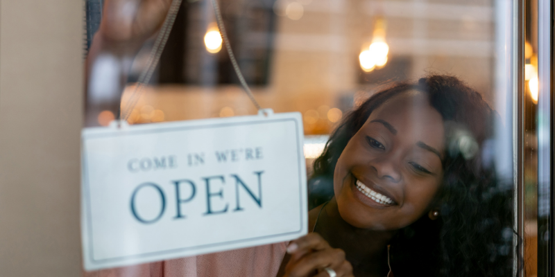 Black woman business owner hanging an open sign on her door.