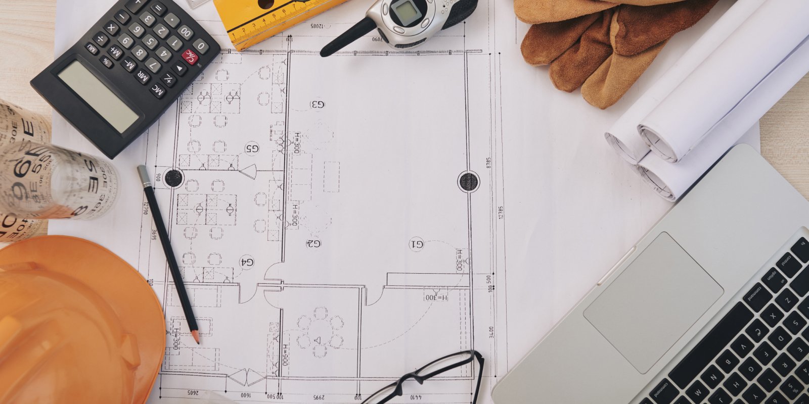 Table with blueprints, calculator, pencil and other materials. 