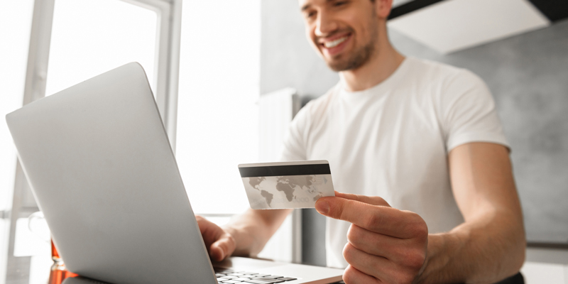 Photo of a man in front of a laptop holding a credit card. 